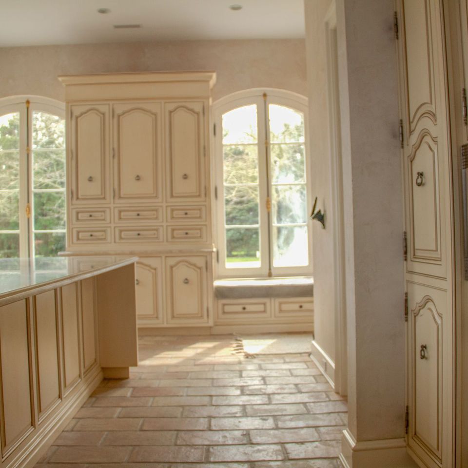 Kitchen with arched windows, cream cabinetry and a terracotta floor